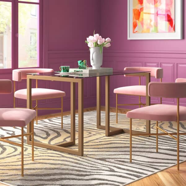 Mesa de jantar amon com tampo em vidro transparente e base em metal dourado juntamente com cadeiras no tecido rosa